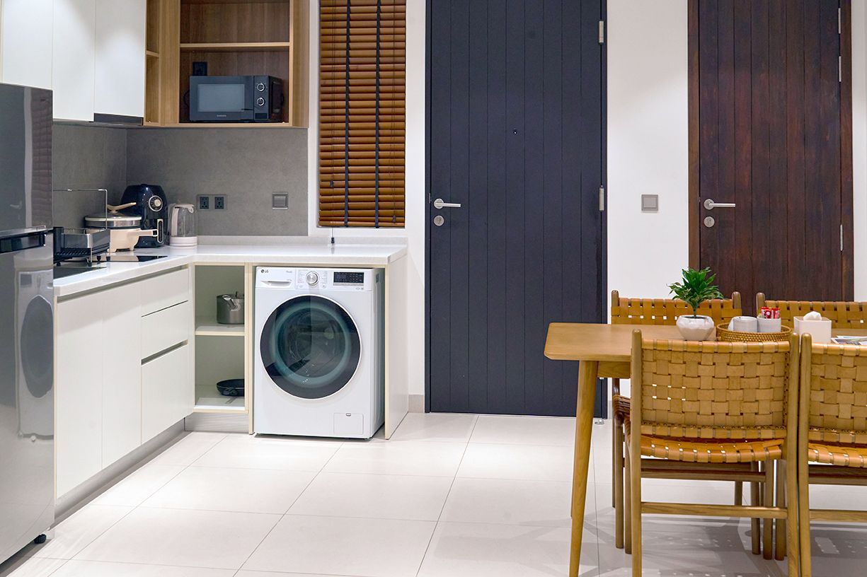 Modern kitchen with white cabinets, laundry machine, wooden dining table, and dark doors.