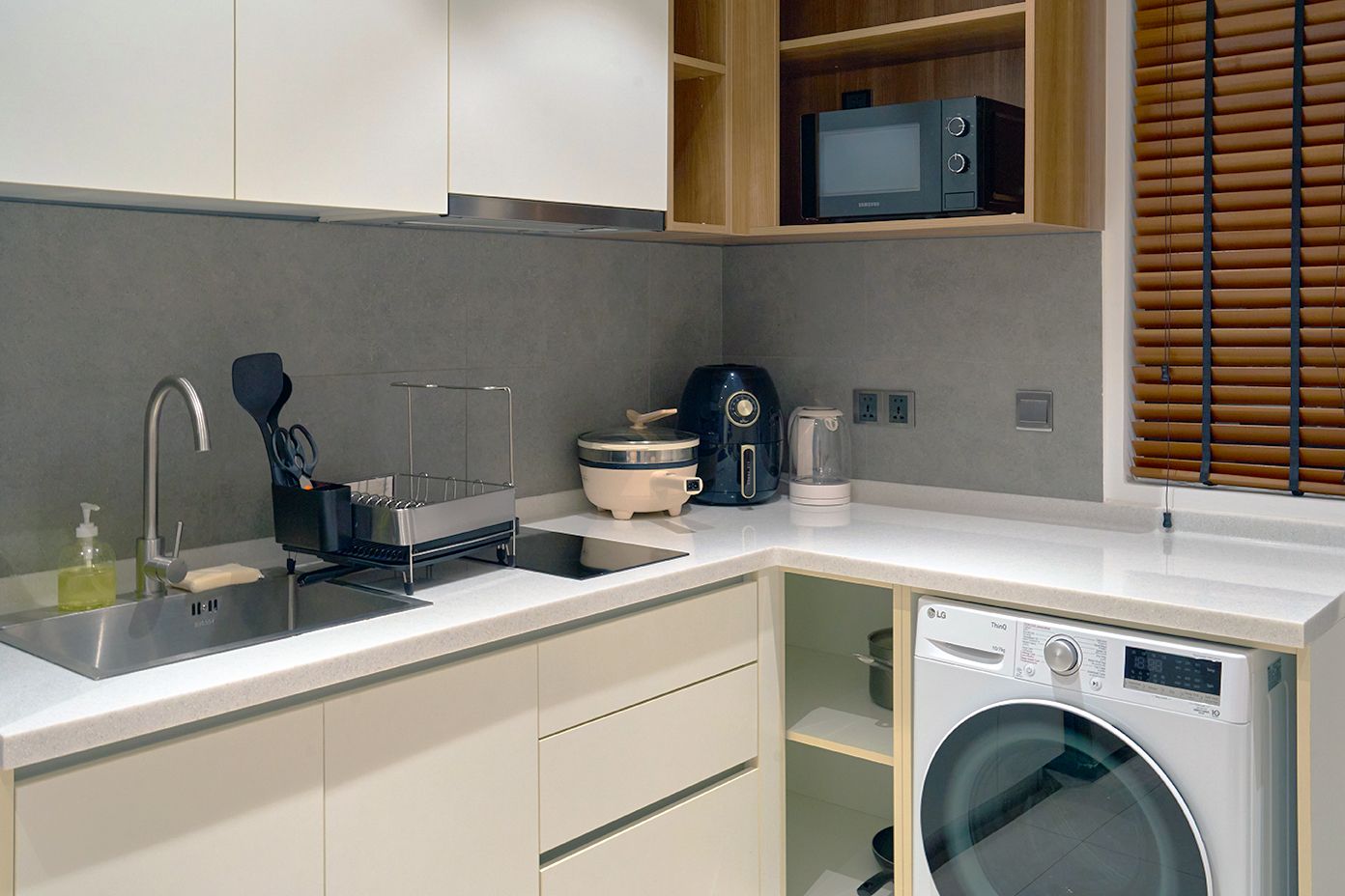 Modern kitchen corner with sink, countertop, microwave, coffee maker, and front-load washer under the counter