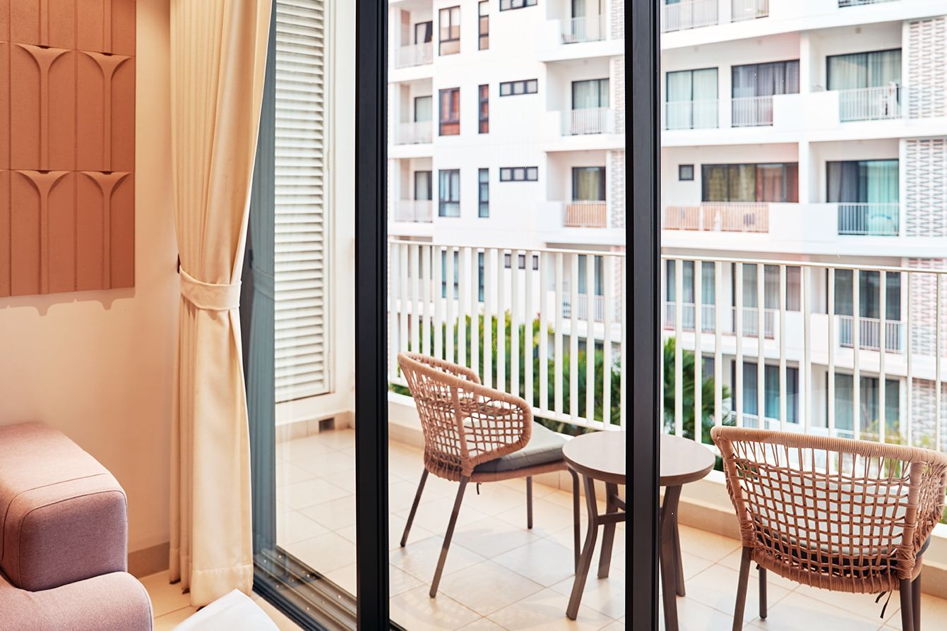 Balcony view from a room with wicker chairs, a small table, and apartment buildings outside