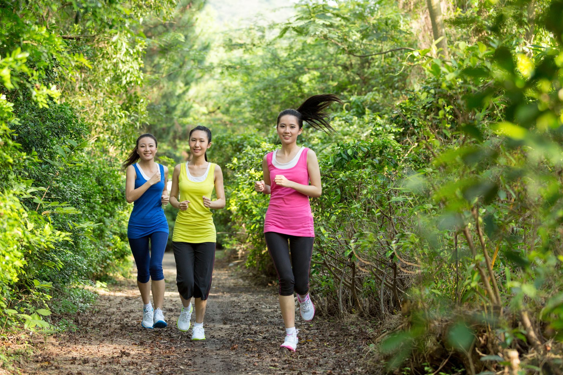 Three hikers walking on a forest trail, with one wearing a pink top and smiling.
