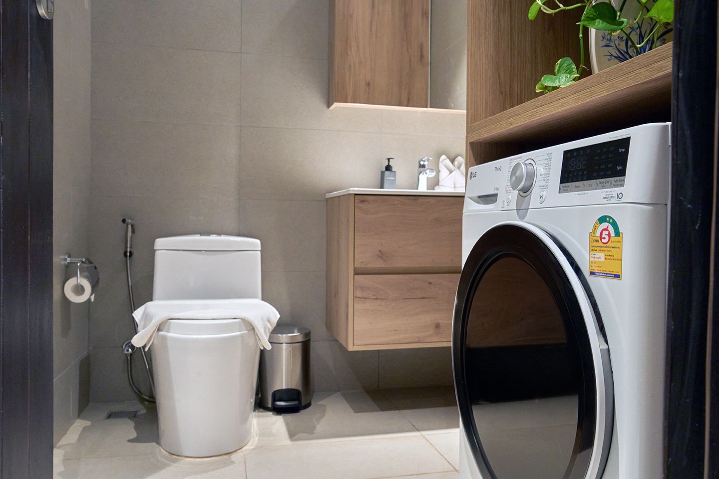 Modern bathroom with toilet, sink cabinet, trash can, and front-loading washer/dryer.