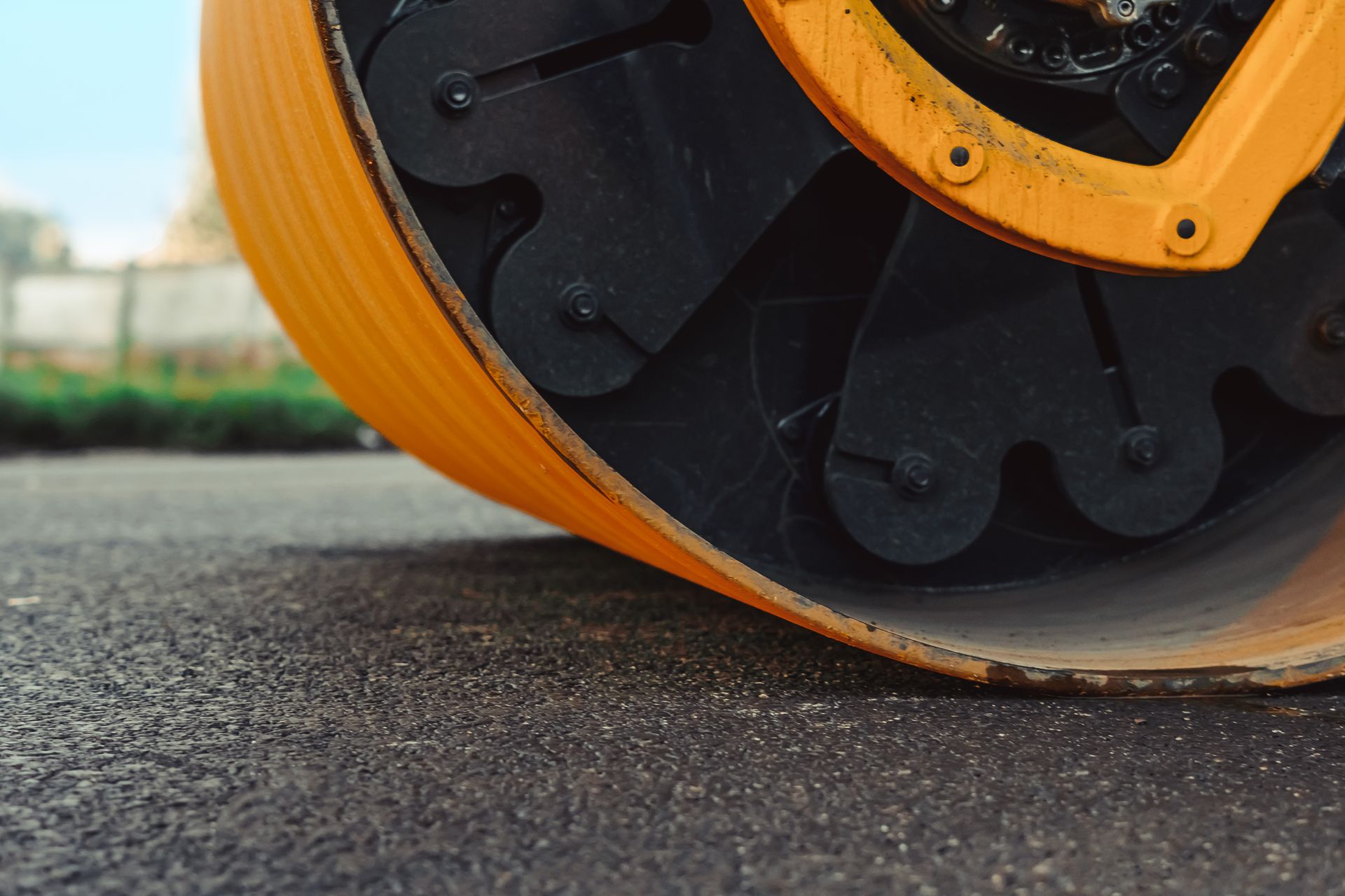 Close-up of a yellow road roller wheel compacting asphalt on a street surface