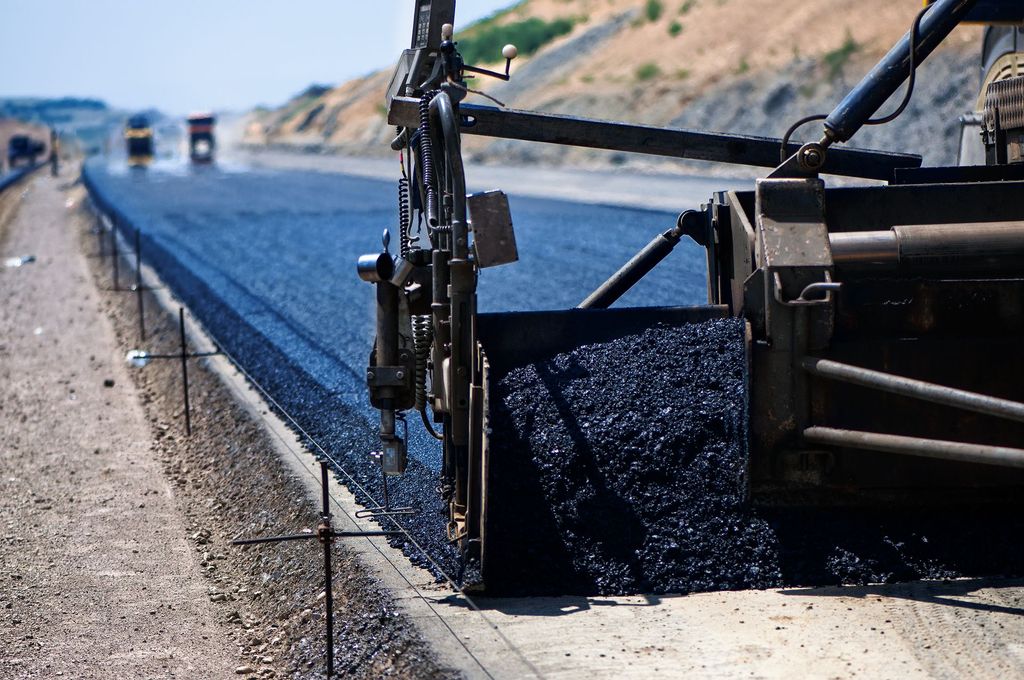 Road paving machine laying fresh asphalt on a highway shoulder