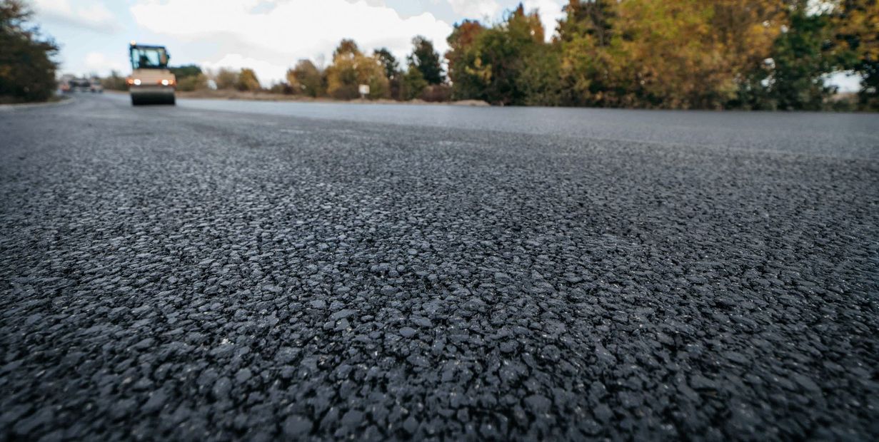 Freshly paved road with a roller in the distance and autumn trees along the sides