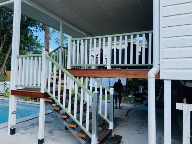 A White House With a Wooden Deck and Stairs Leading Up to It — NGK Constructions In Freshwater, QLD