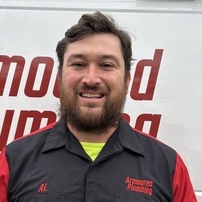 Smiling mechanic in a black and red uniform standing in front of a logo backdrop