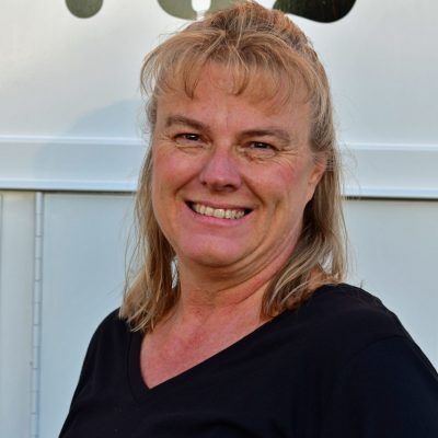 Smiling woman in a black top standing outdoors by a white vehicle.