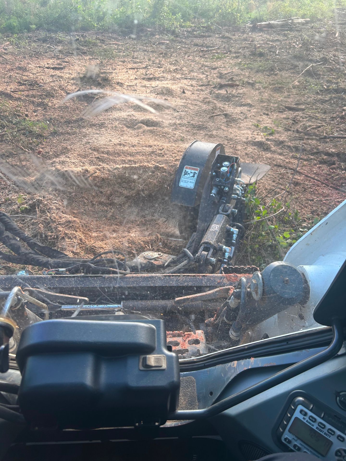 Bobcat skid-steer grinder grinding a tree stump in a dirt clearing.