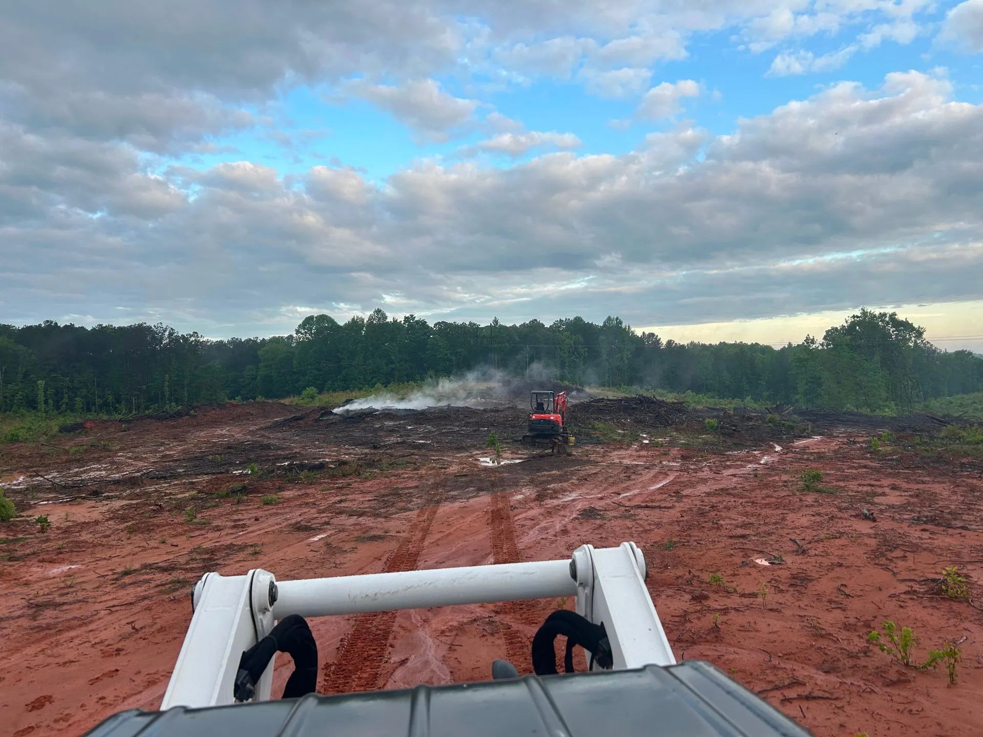 View from a vehicle on a muddy dirt road toward a red off-road vehicle under a cloudy sky