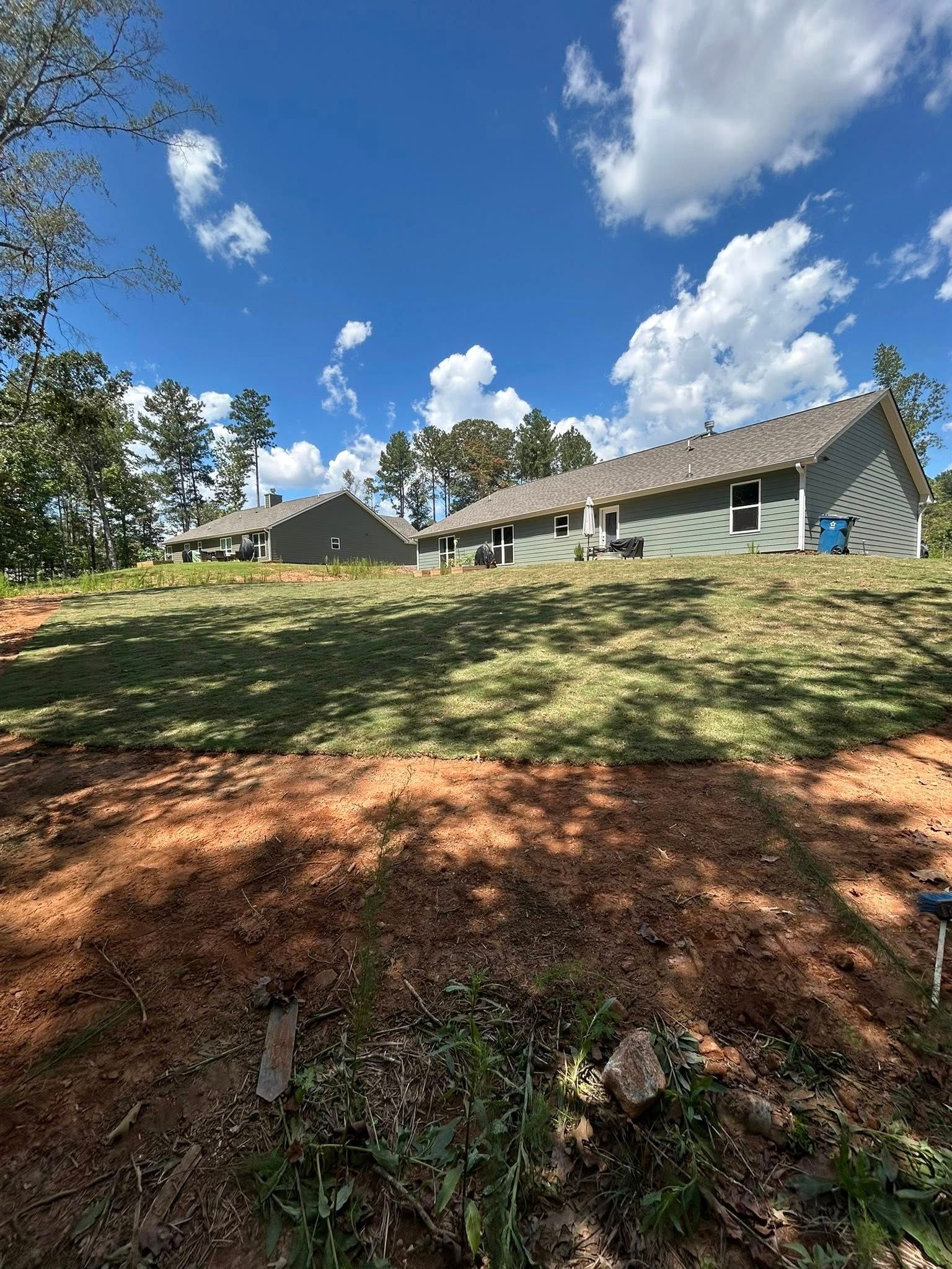 Green buildings on a grassy hill under a blue sky with clouds.