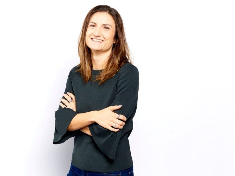 Smiling woman with crossed arms wearing a dark long-sleeve top against a white background