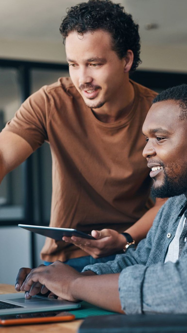 Two men are sitting at a table looking at a tablet.