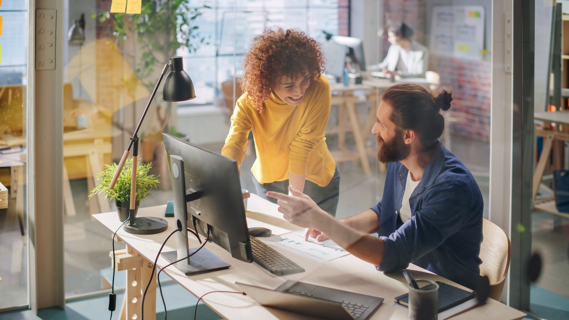 A man and a woman are looking at a computer screen in an office.