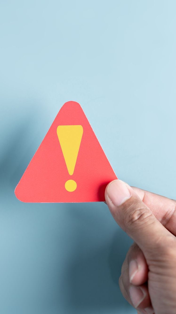 A hand is holding a red triangle with an exclamation point on it.