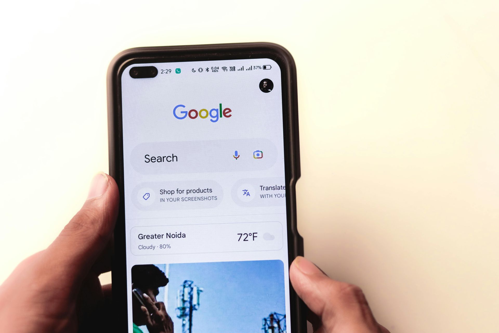 Hands holding a smartphone showing the Google search homepage on a white background
