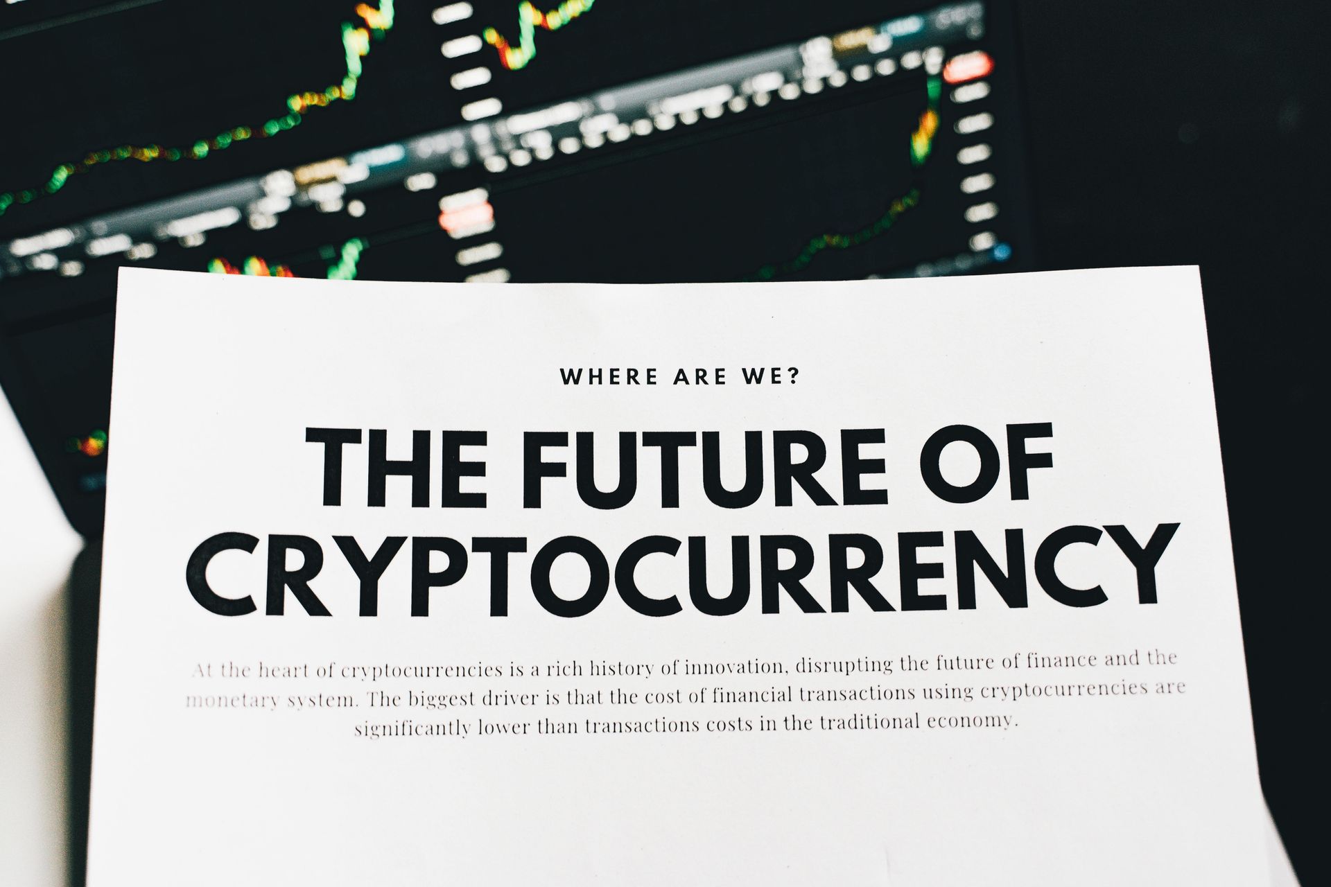 Printed page titled “The Future of Cryptocurrency” over a blurred stock chart display