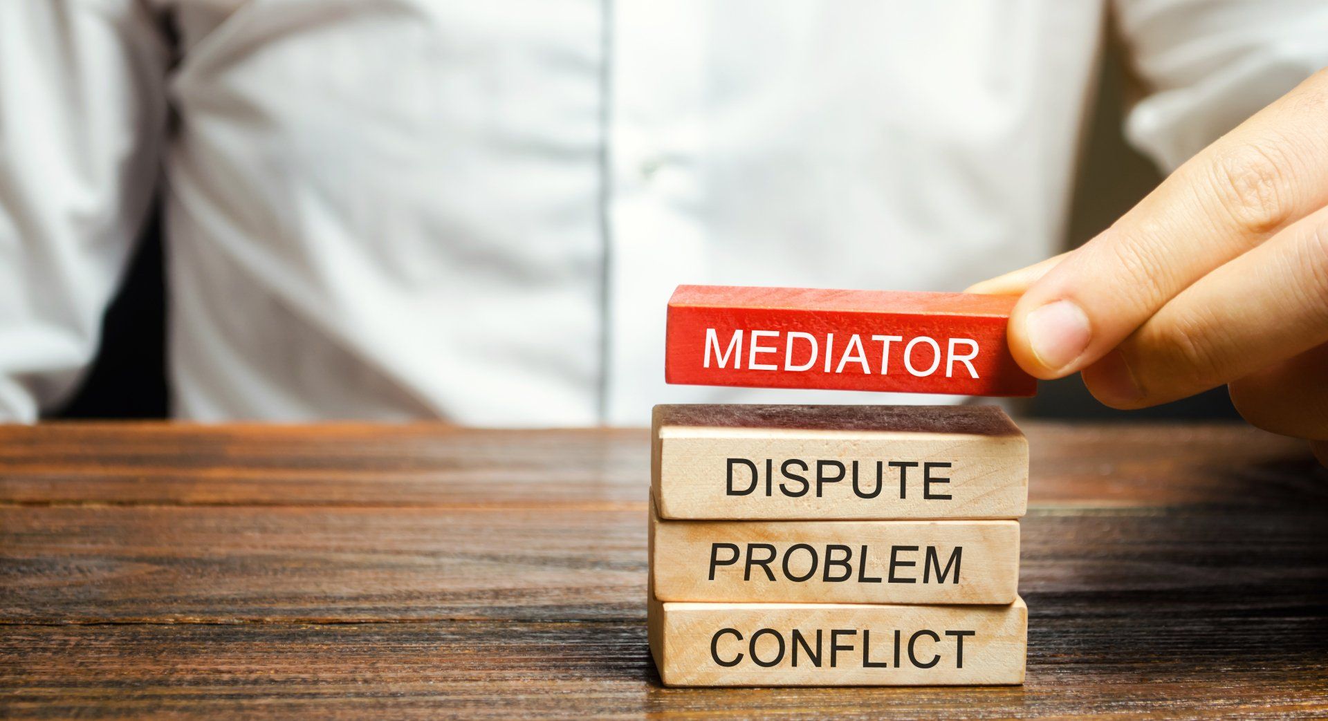 A person is stacking wooden blocks with the words mediator , dispute problem , conflict written on them.