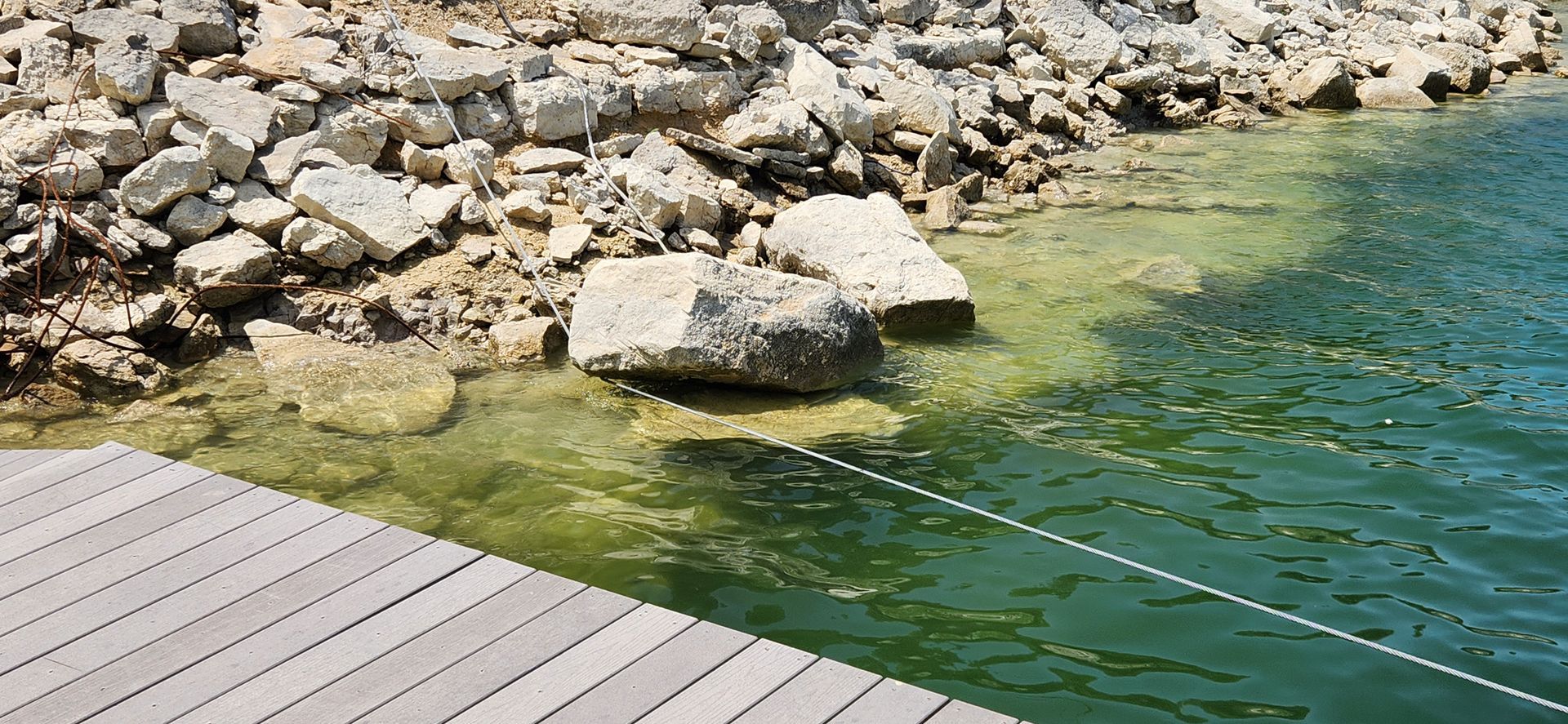 Rocks line the edge of a body of water. A wooden dock sits in the bottom left corner.