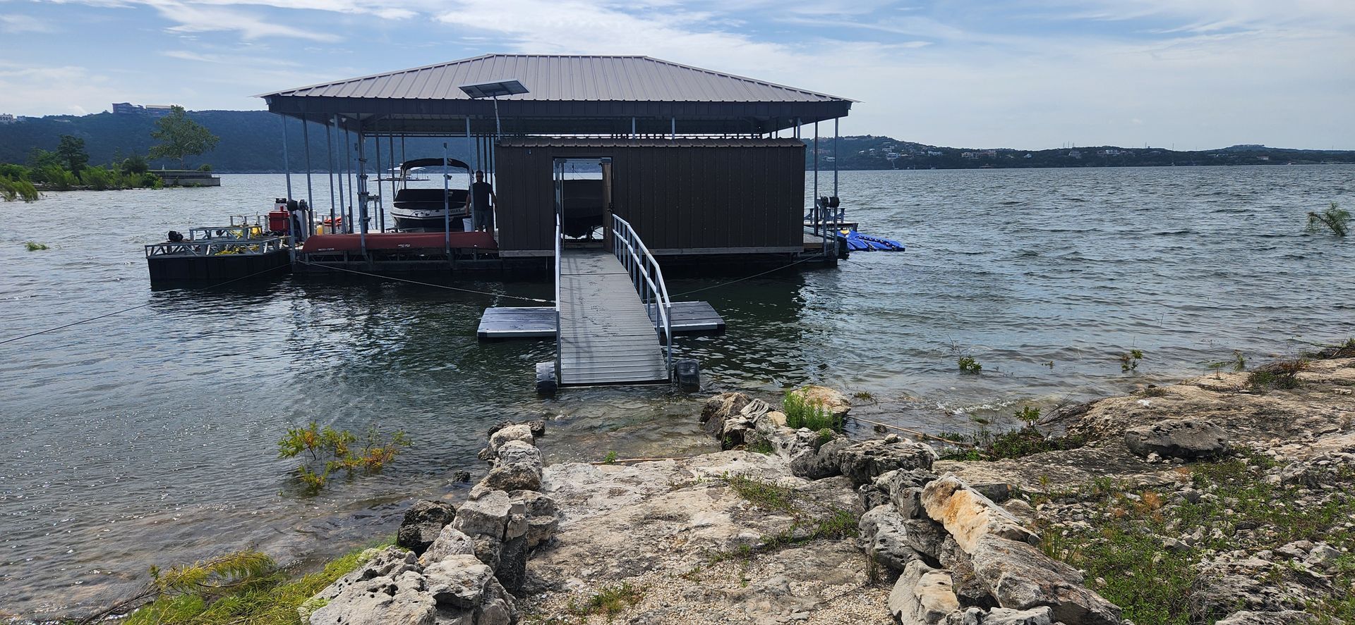 A dock on a lake with a ramp leading to the shore. The dock has a roof and a boat inside.