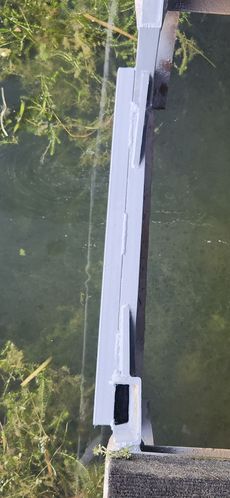 Metal structure over water, possibly a bridge or dam. Green vegetation visible.