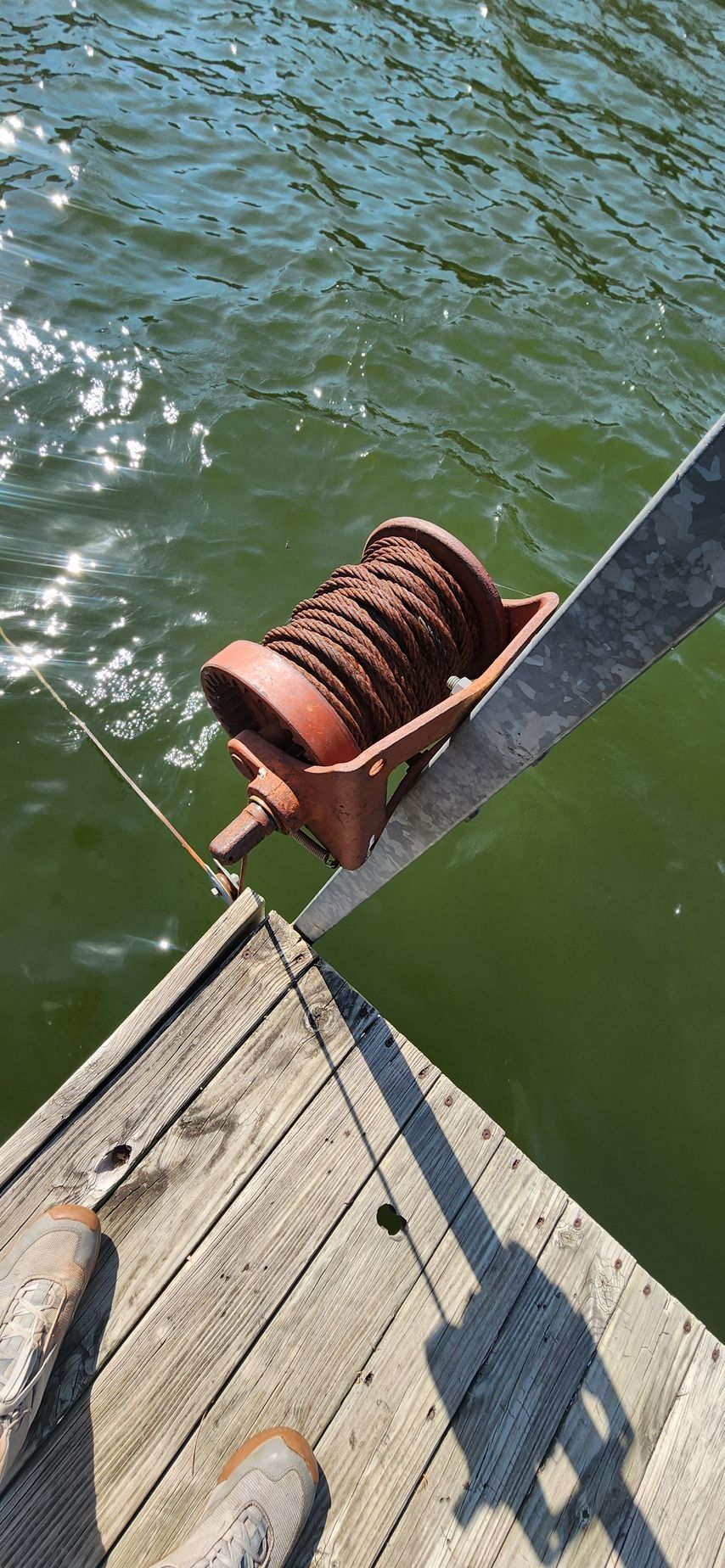 An old, rusty winch on a wooden dock next to green water.
