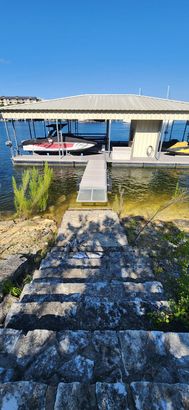 Stone steps leading to a boat dock with a boat under a covered roof on a sunny day.