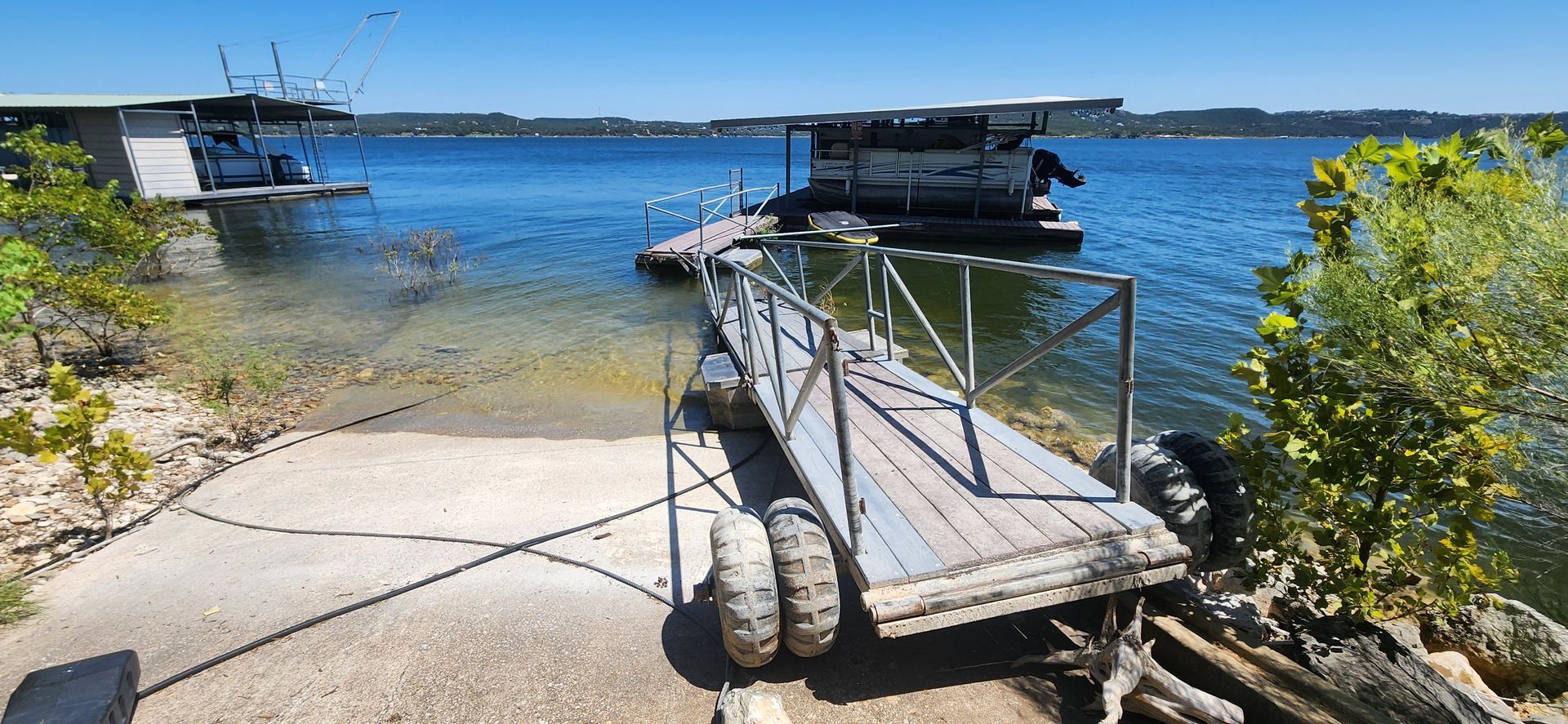 A boat ramp leading to a lake with docks and a boat on a sunny day.