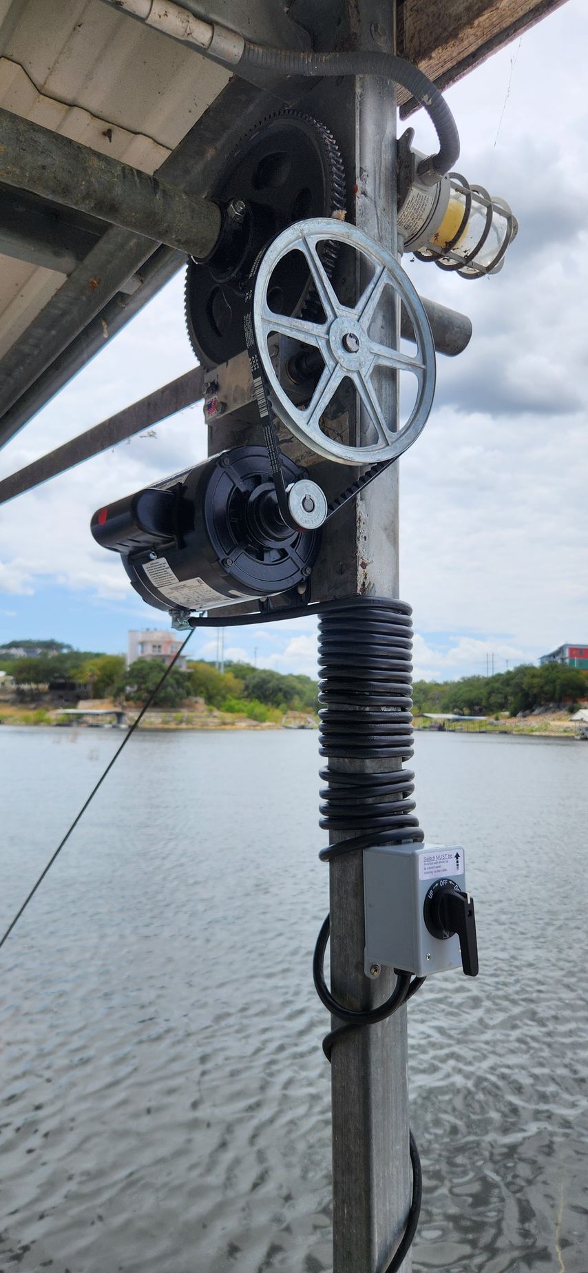 A mechanical lift system on a pier with gears, a motor, and a light. The water is in the background.
