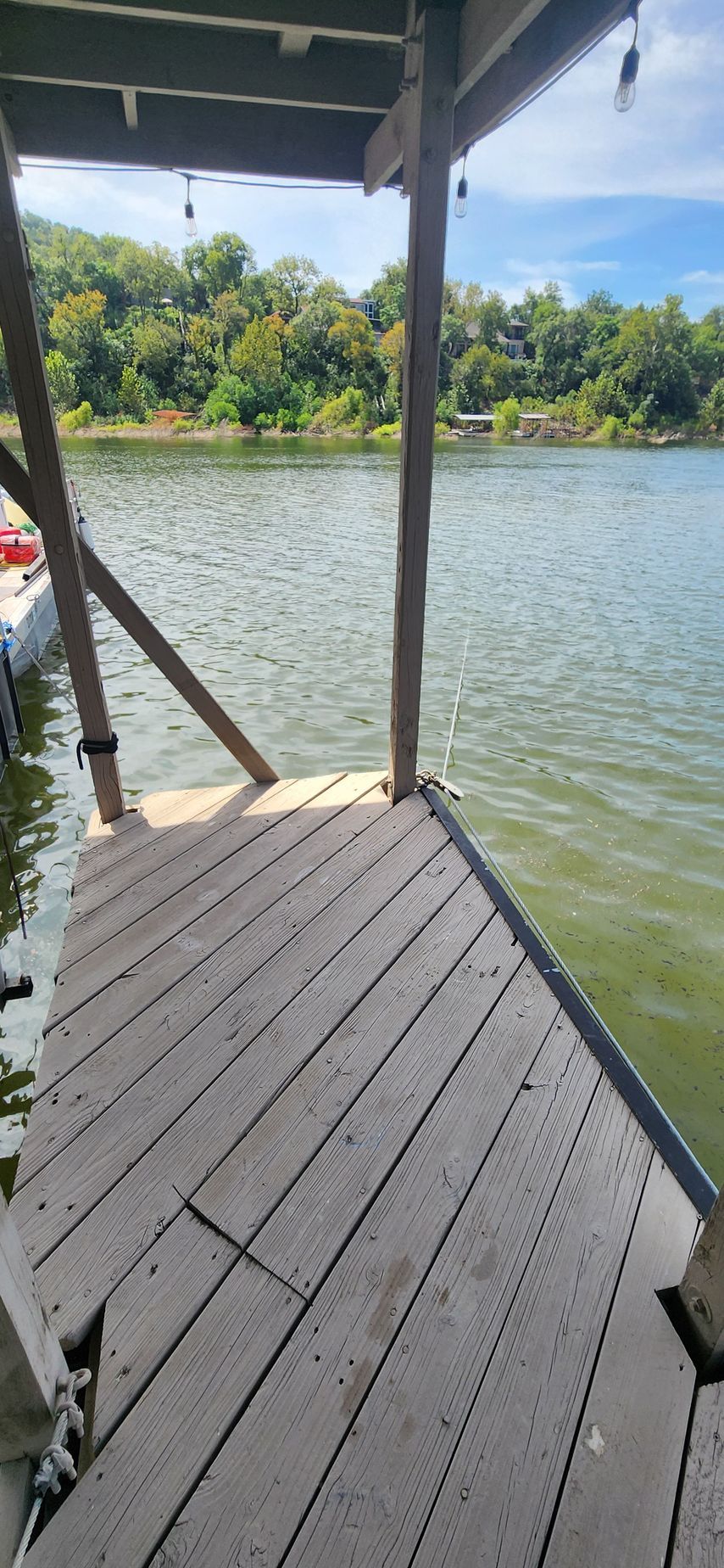 Wooden dock with lake in the background, under a covered structure with trees and sky.