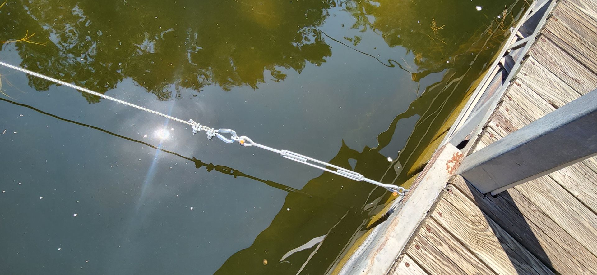 View of water reflecting sunlight, with ropes and a wooden dock.