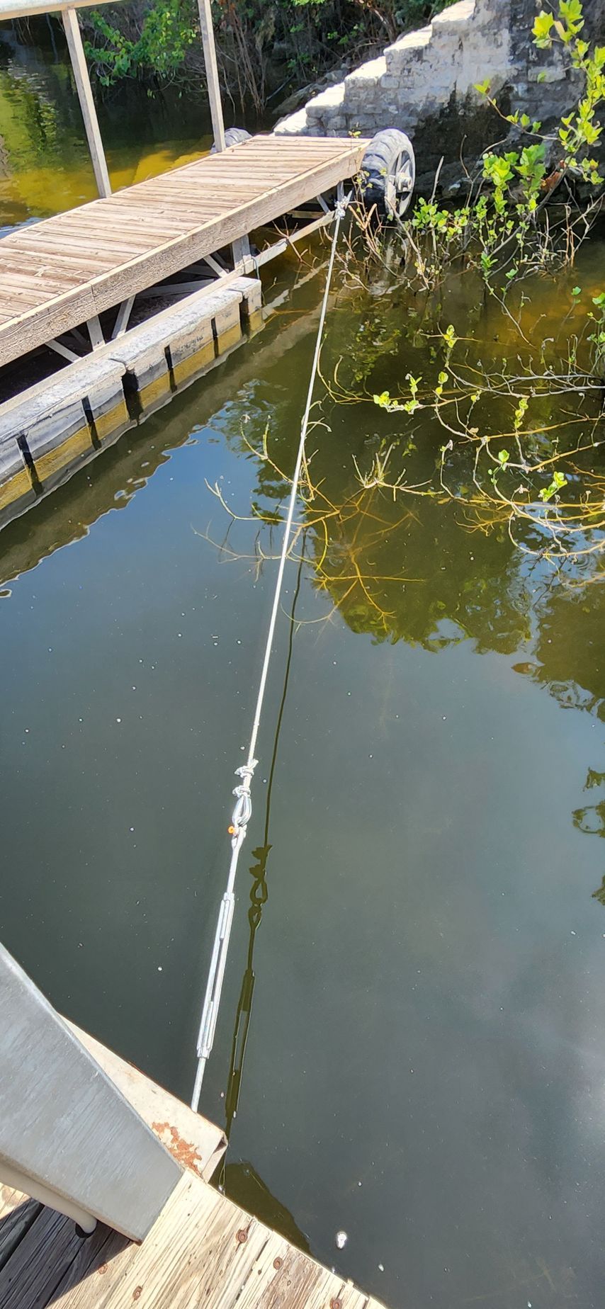 Wooden dock with a rope extending into dark water, possibly a lake.