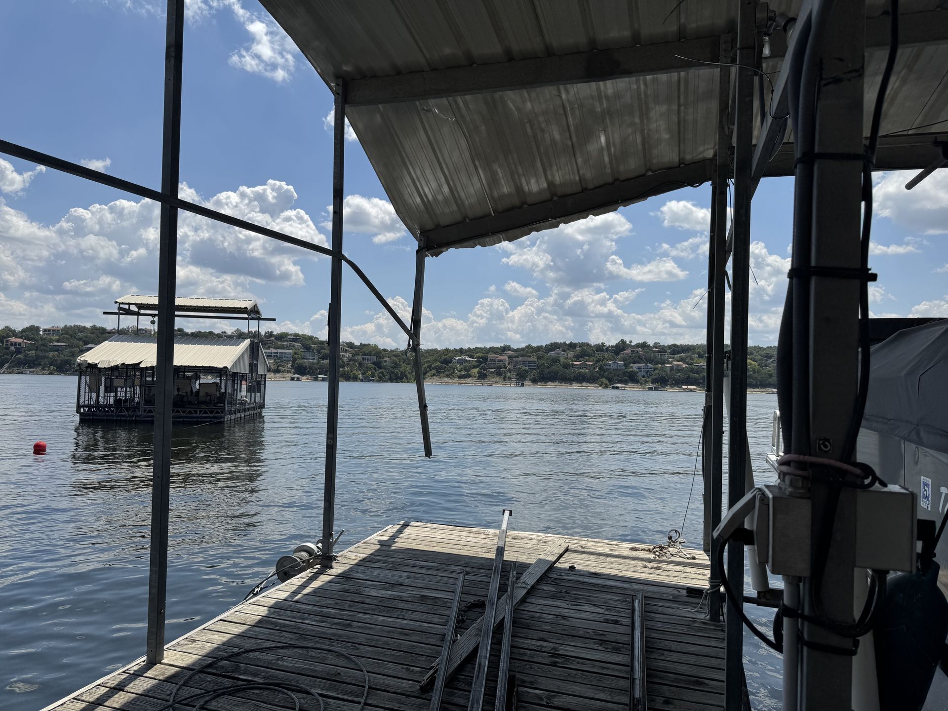 A waterside view of a lake from a boat dock with a visible covered dock in the distance and a clear sky.