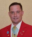 A man wearing a red jacket and tie with pins on it