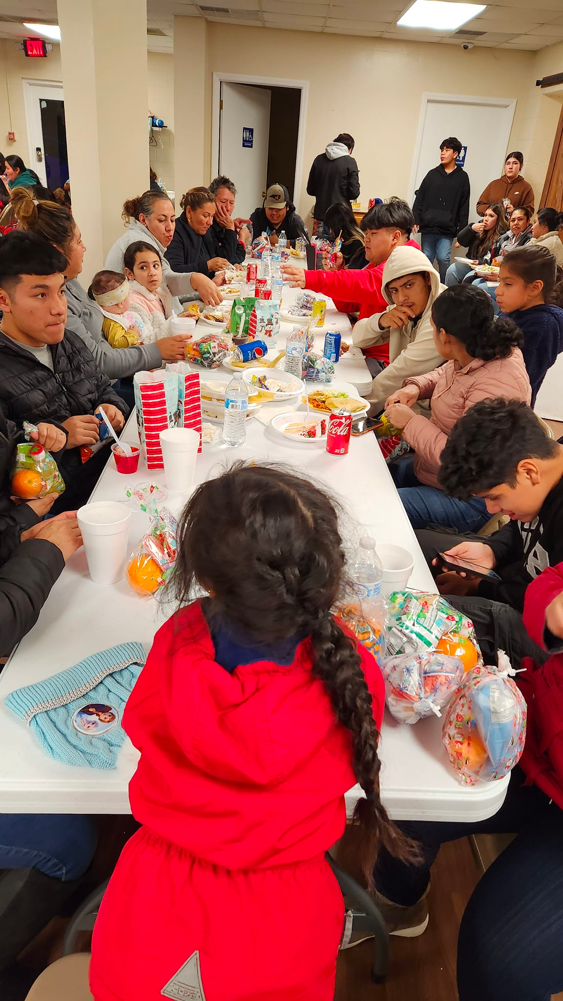A little girl in a red jacket is sitting at a table with other people