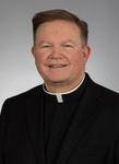 A man in a suit and a clergy collar smiles for the camera
