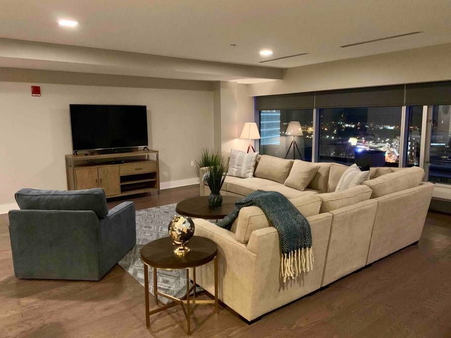 Modern living room with large beige sectional, city view, TV, and blue armchair.