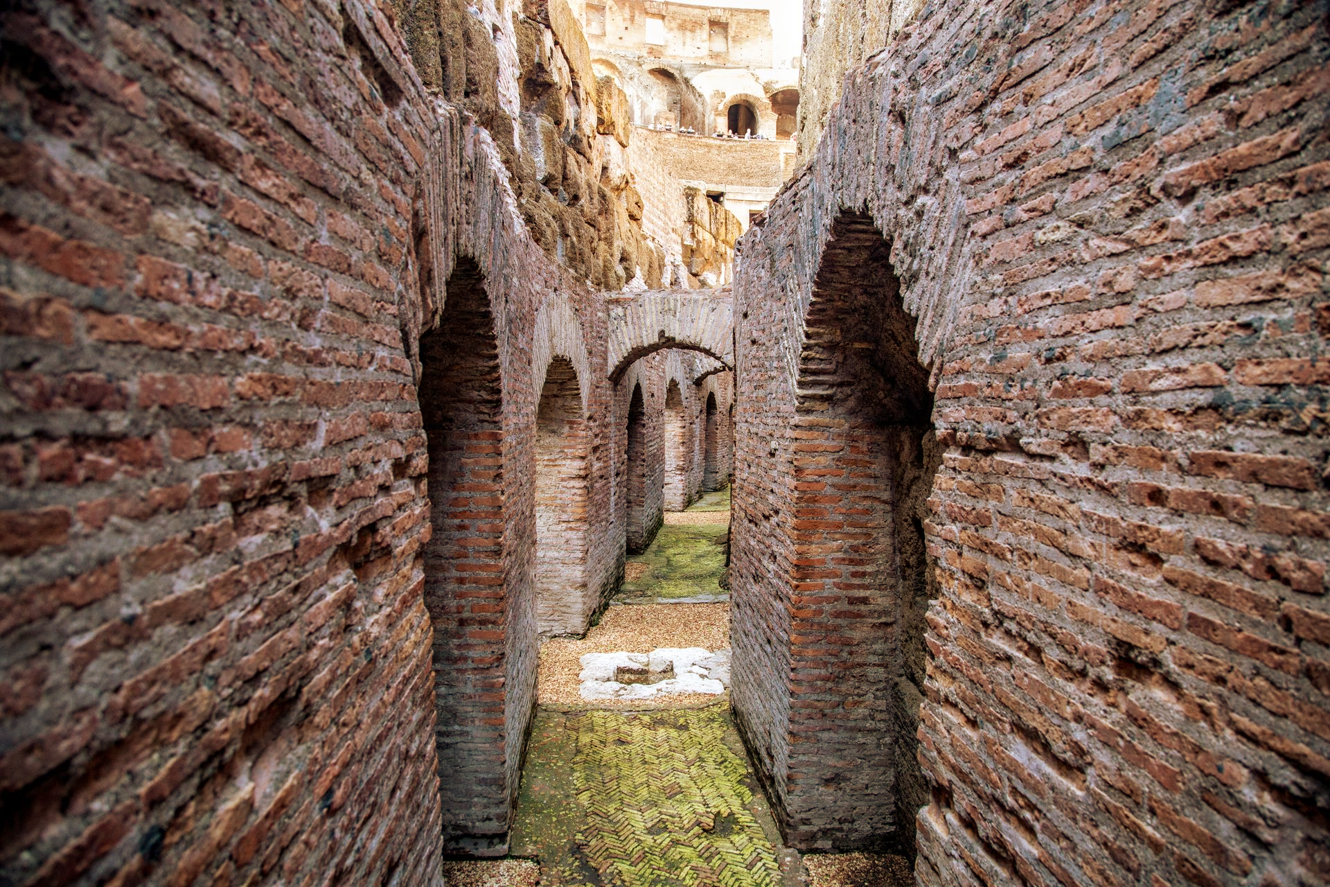 Arched brick corridors inside the Colosseum in Rome, with sunlight streaming down.