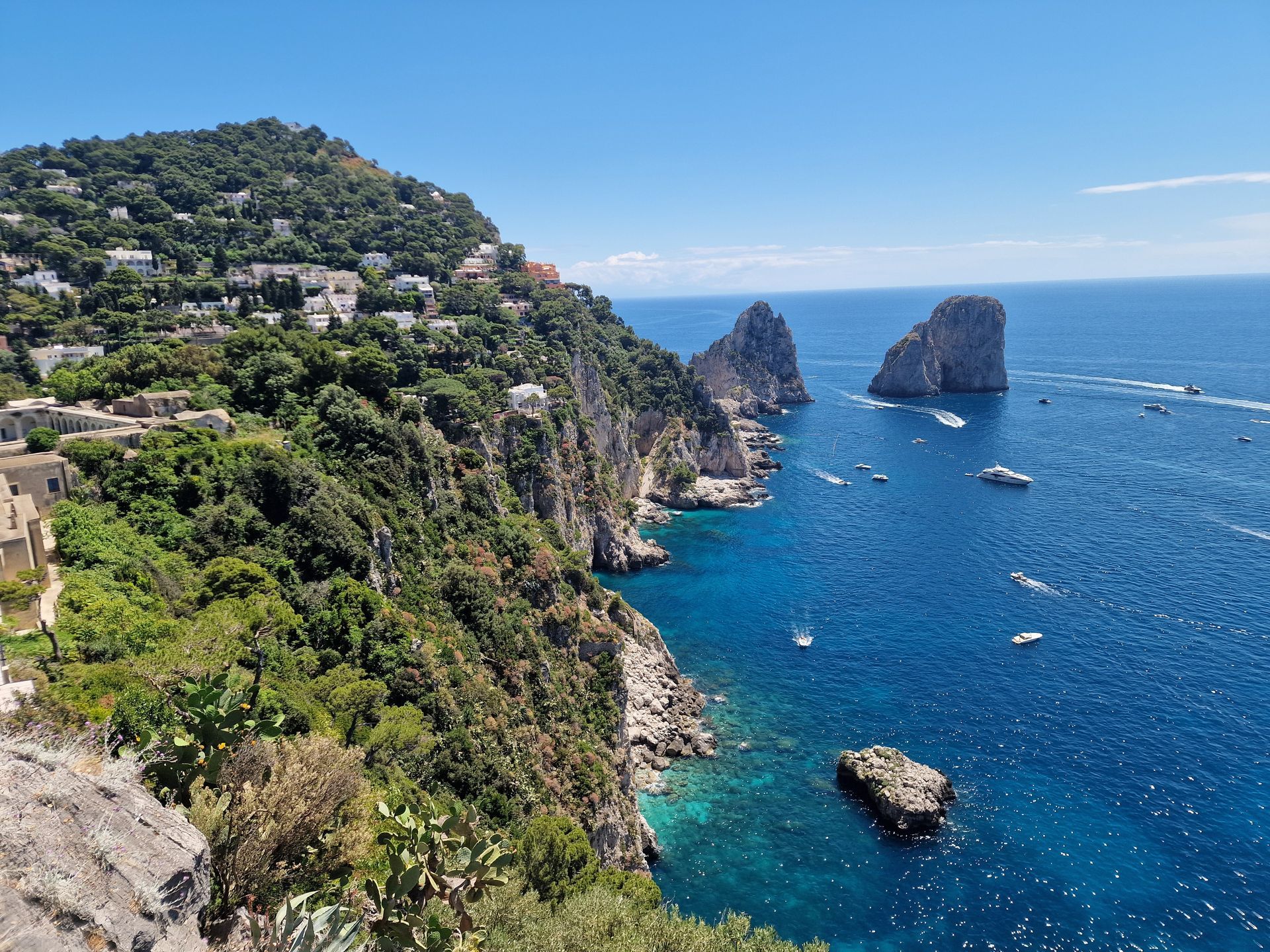 Coastal cliffs with lush greenery overlooking a deep blue sea and two rocky sea stacks.