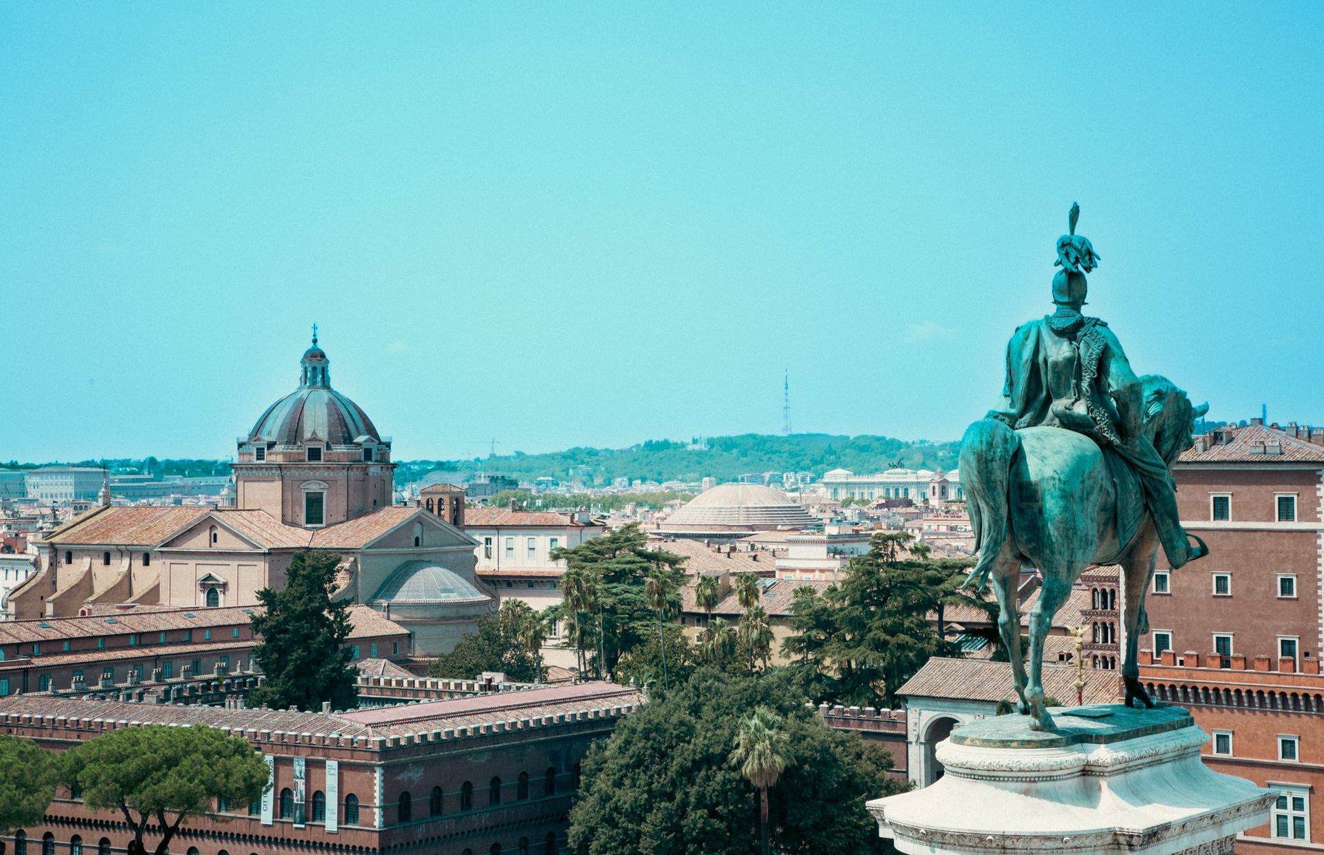 Equestrian statue overlooking Rome cityscape with dome and other buildings under blue sky.