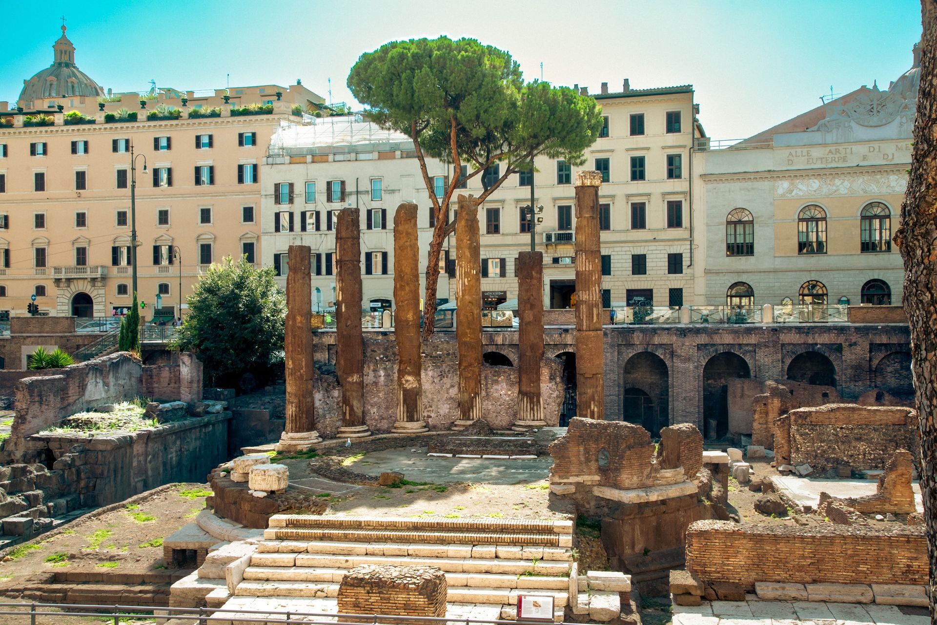 Ruins of ancient Roman forum with Trajan's Column, church, and surrounding buildings under a blue sky.