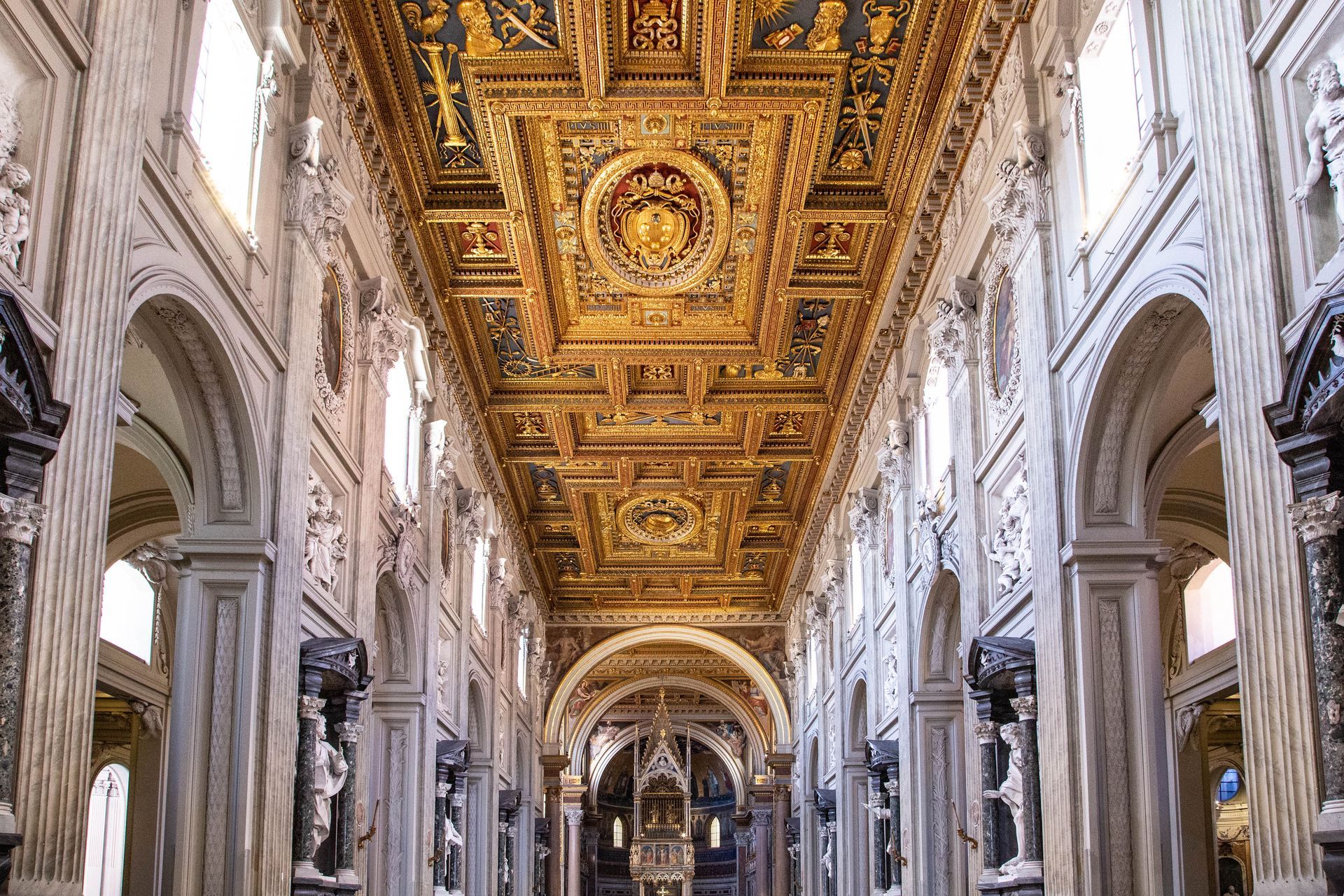 Ornate cathedral interior with gilded ceiling, marble arches, and a long central nave