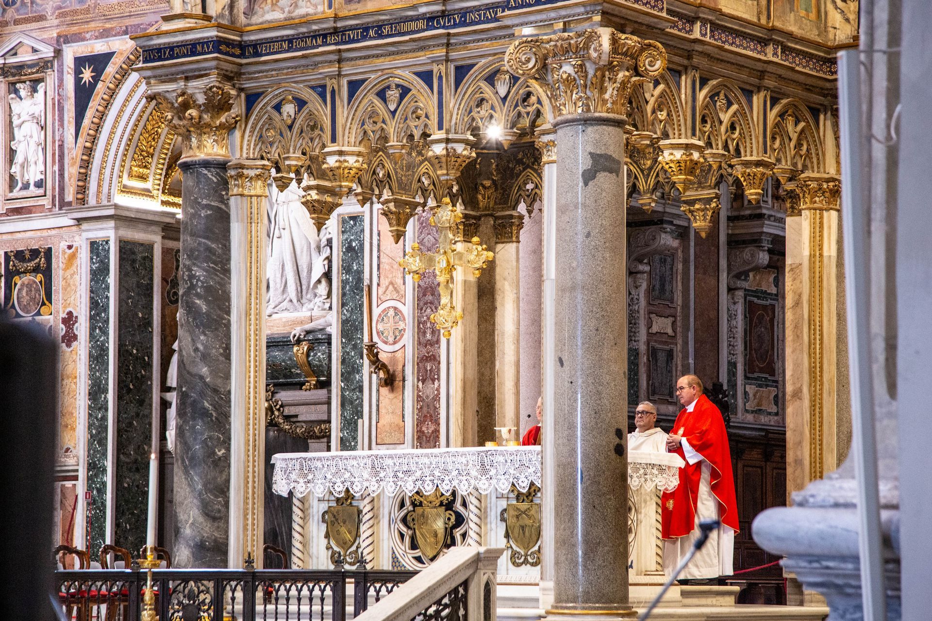 Ornate church altar with marble columns; a person in red stands near the altar under gold decorations.
