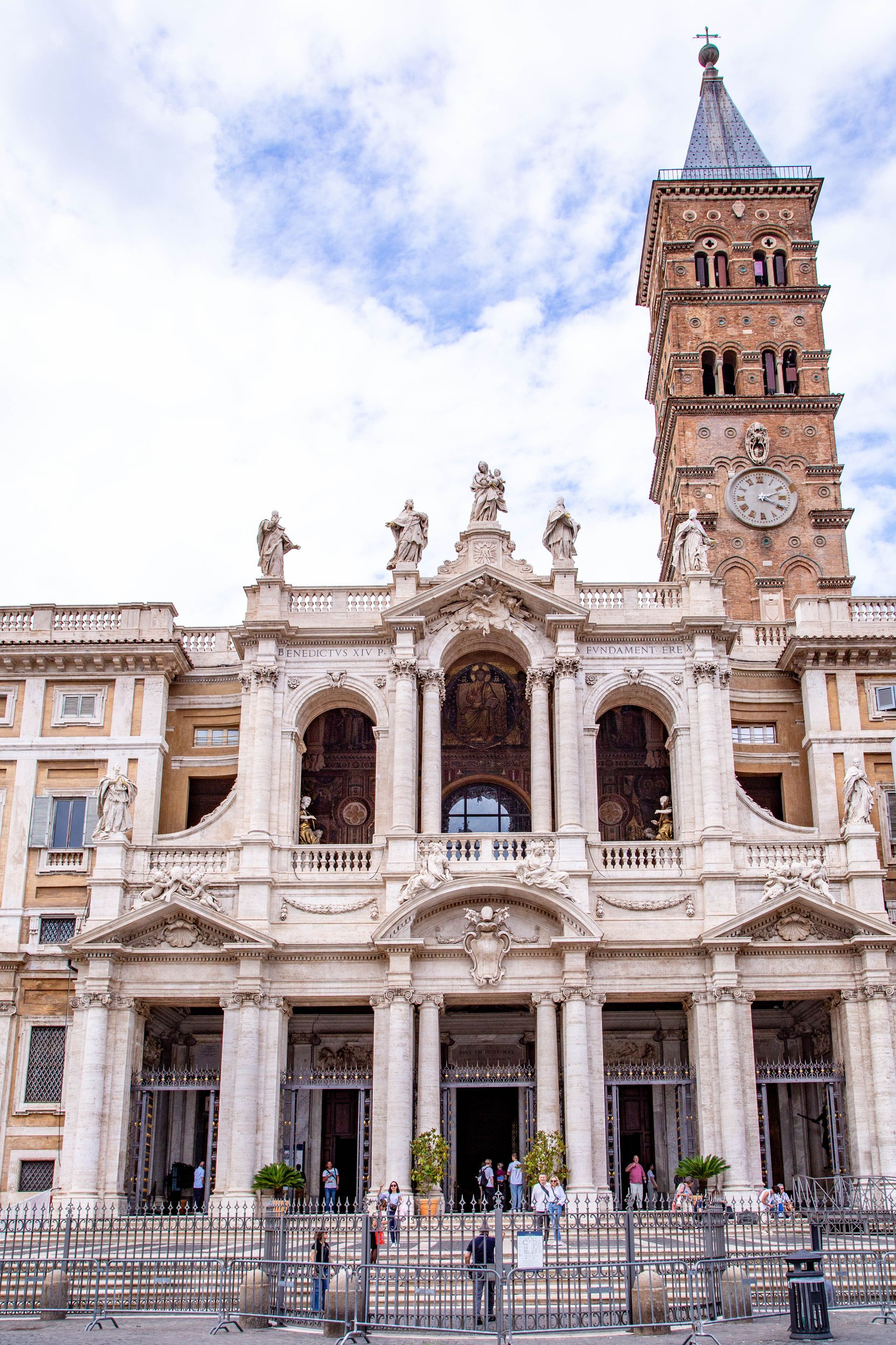 Baroque church facade with statues and a tall bell tower against a blue sky.