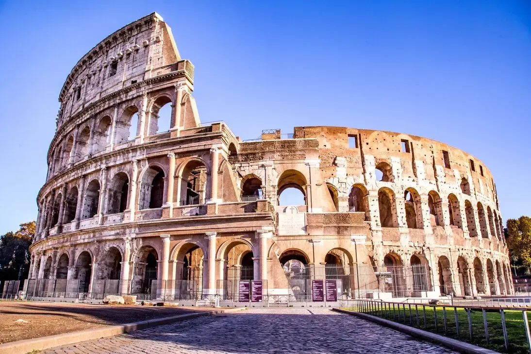 Colosseum in Rome, Italy, with arches, columns, and partially destroyed walls, under a clear blue sky.