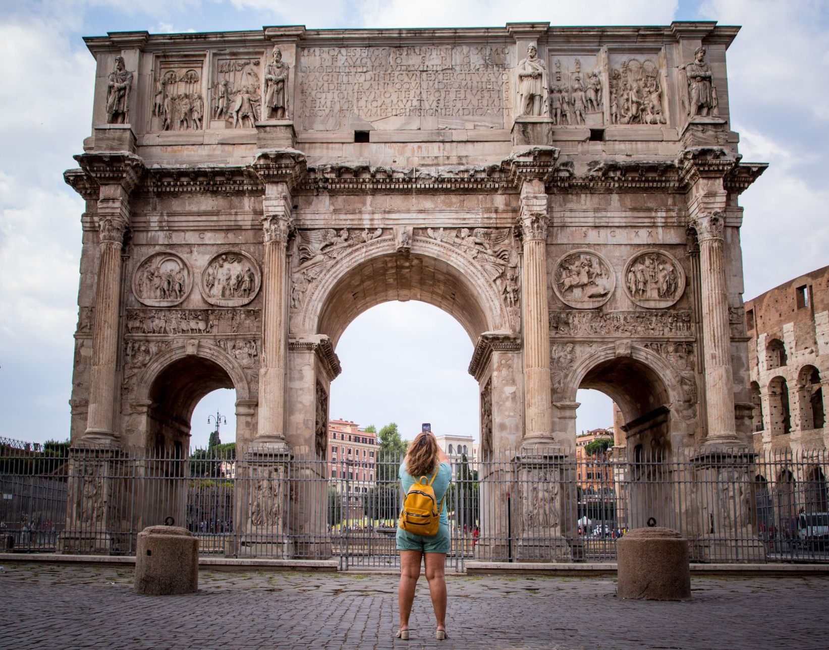 Woman with yellow backpack takes photo of Arch of Constantine, Rome.