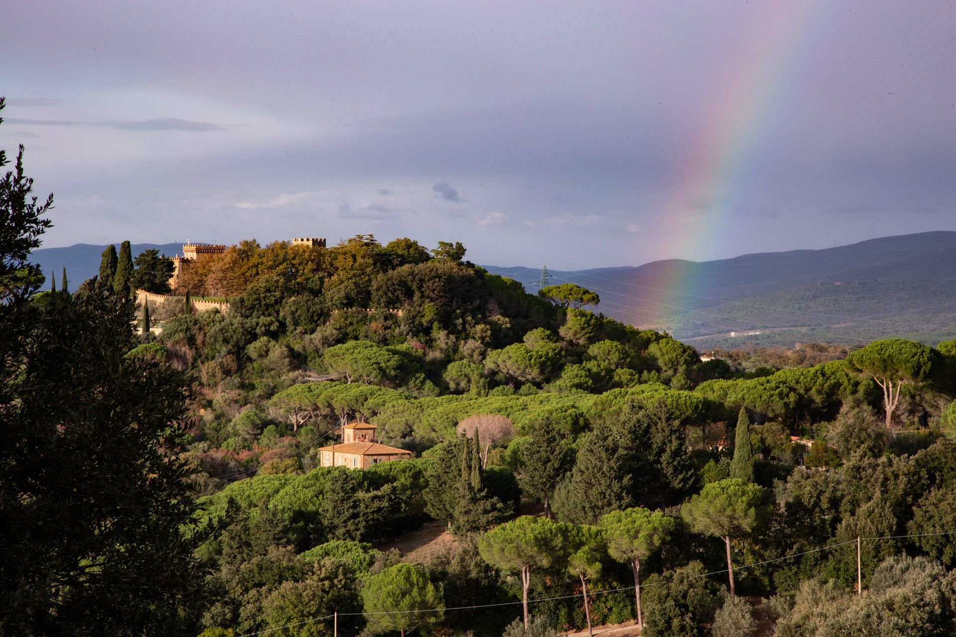 Lush green hillside with houses and a faint rainbow over a distant mountain valley