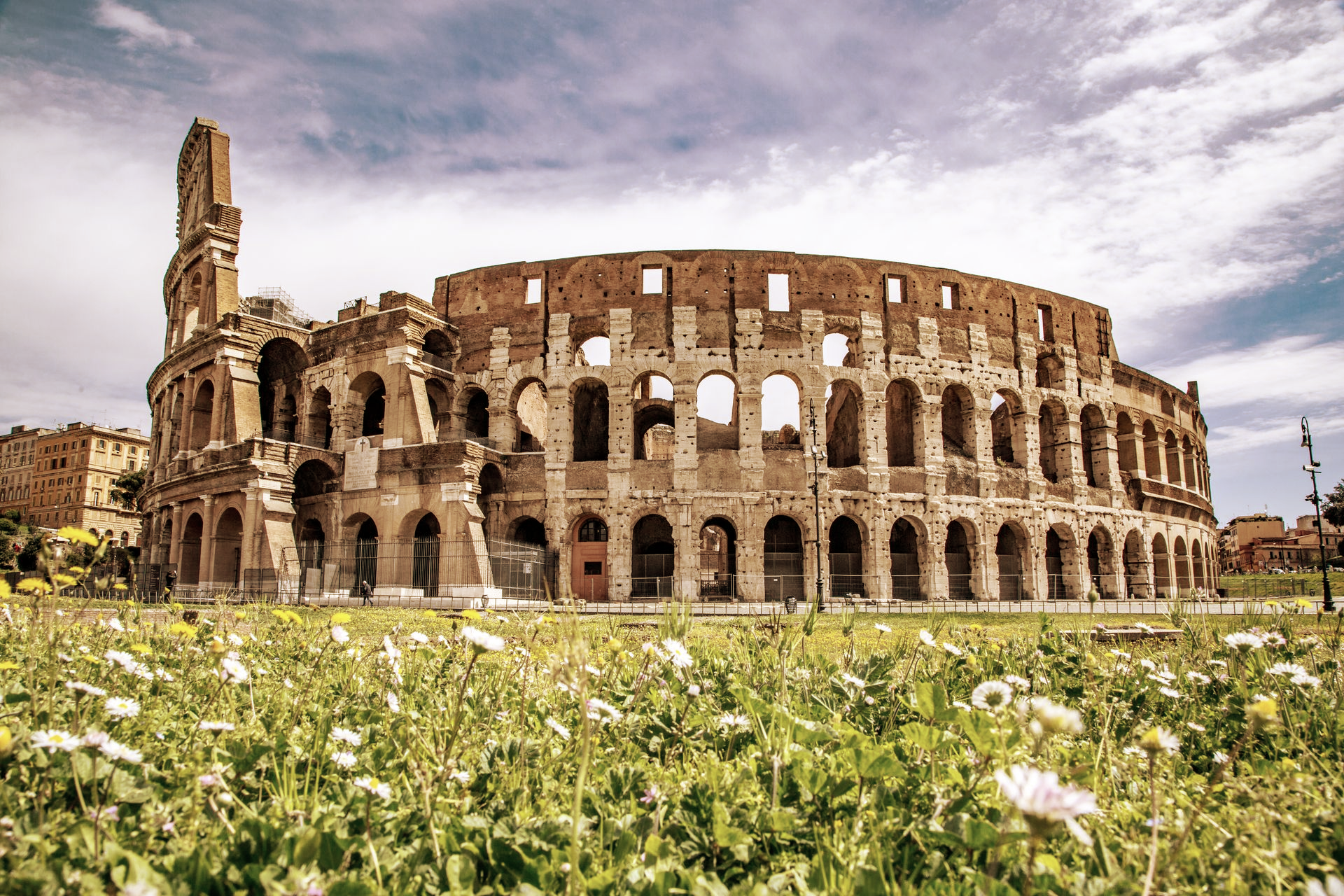 Colosseum in Rome, Italy, a large, weathered stone amphitheater with arched openings, set against a cloudy sky.