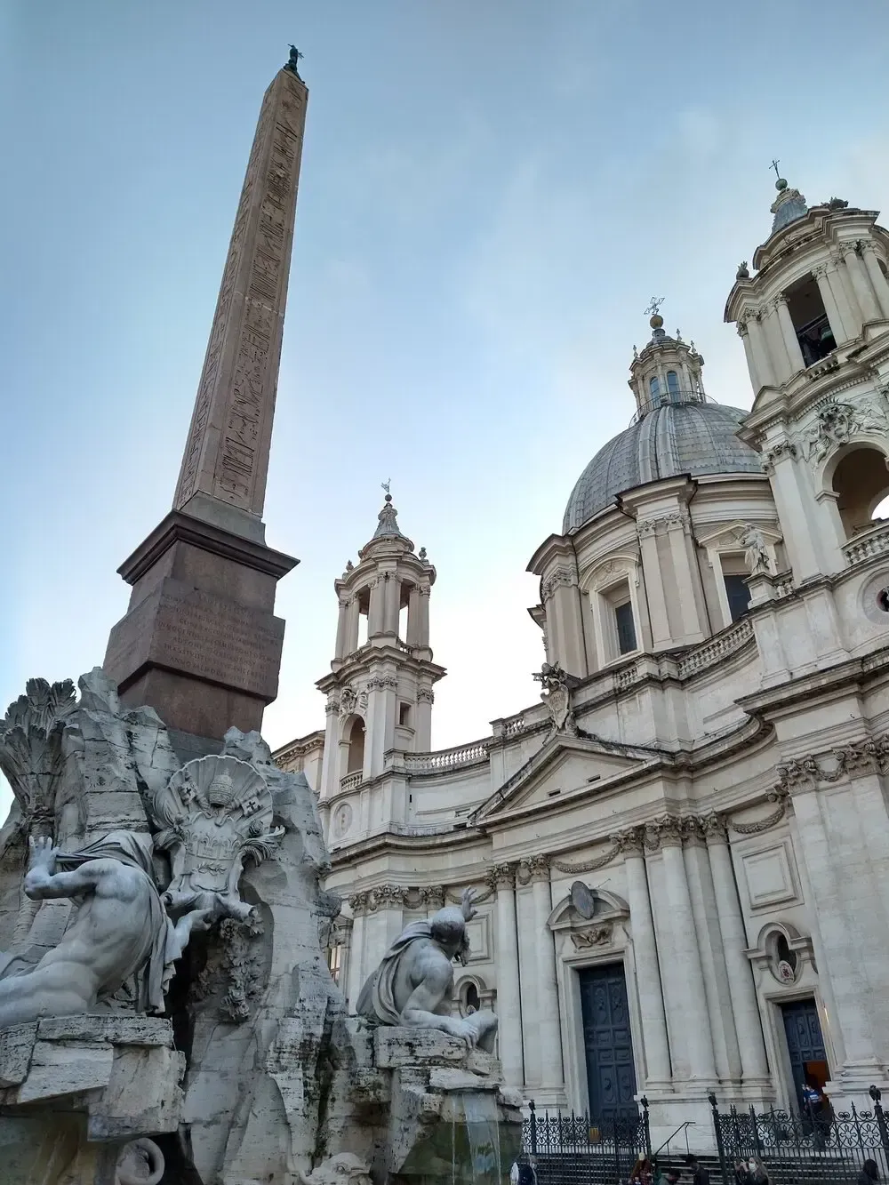 Obelisk, fountain, and church in Piazza Navona, Rome, against a clear, blue sky.