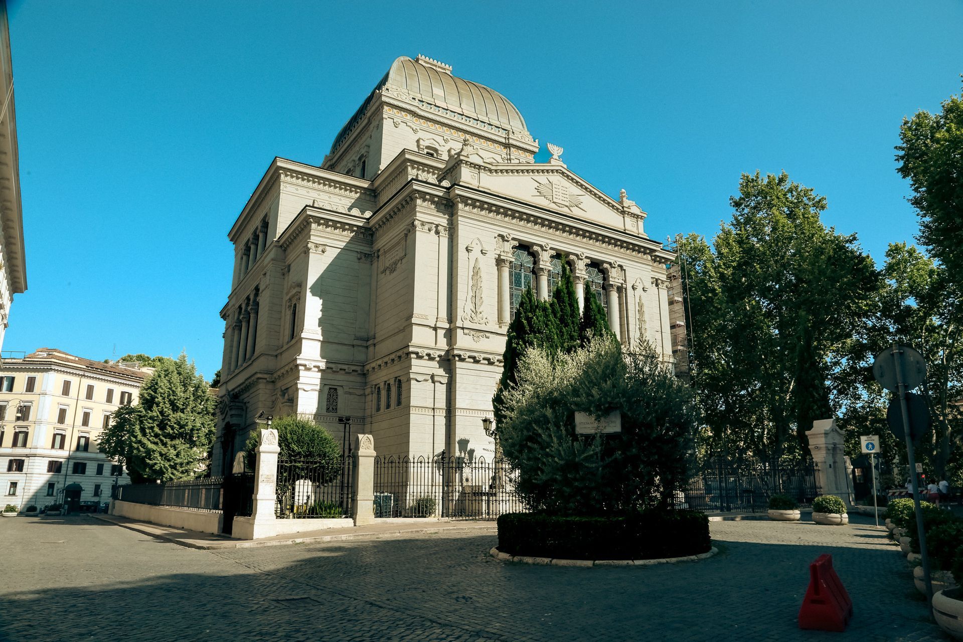 A large, light-colored synagogue with a domed roof in Rome, Italy, on a sunny day.