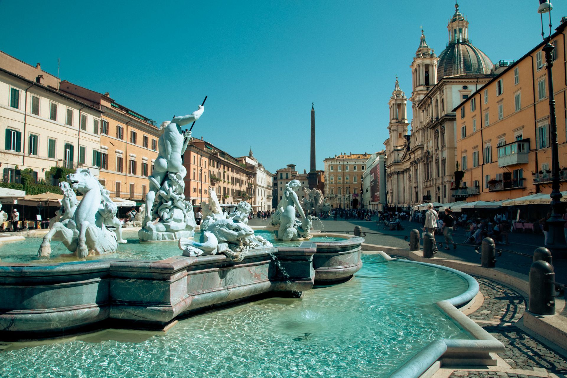 Fountain in Piazza Navona, Rome, with sculptures, buildings, and clear blue sky.